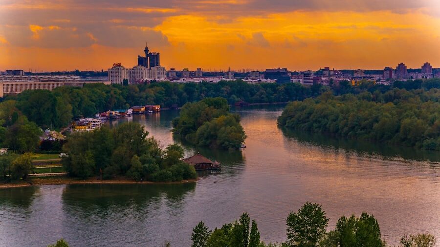 Puesta de sol sobre la ciudad y el río con islas verdes, paisaje pintoresco con reflejo en el agua y cielo brillante.