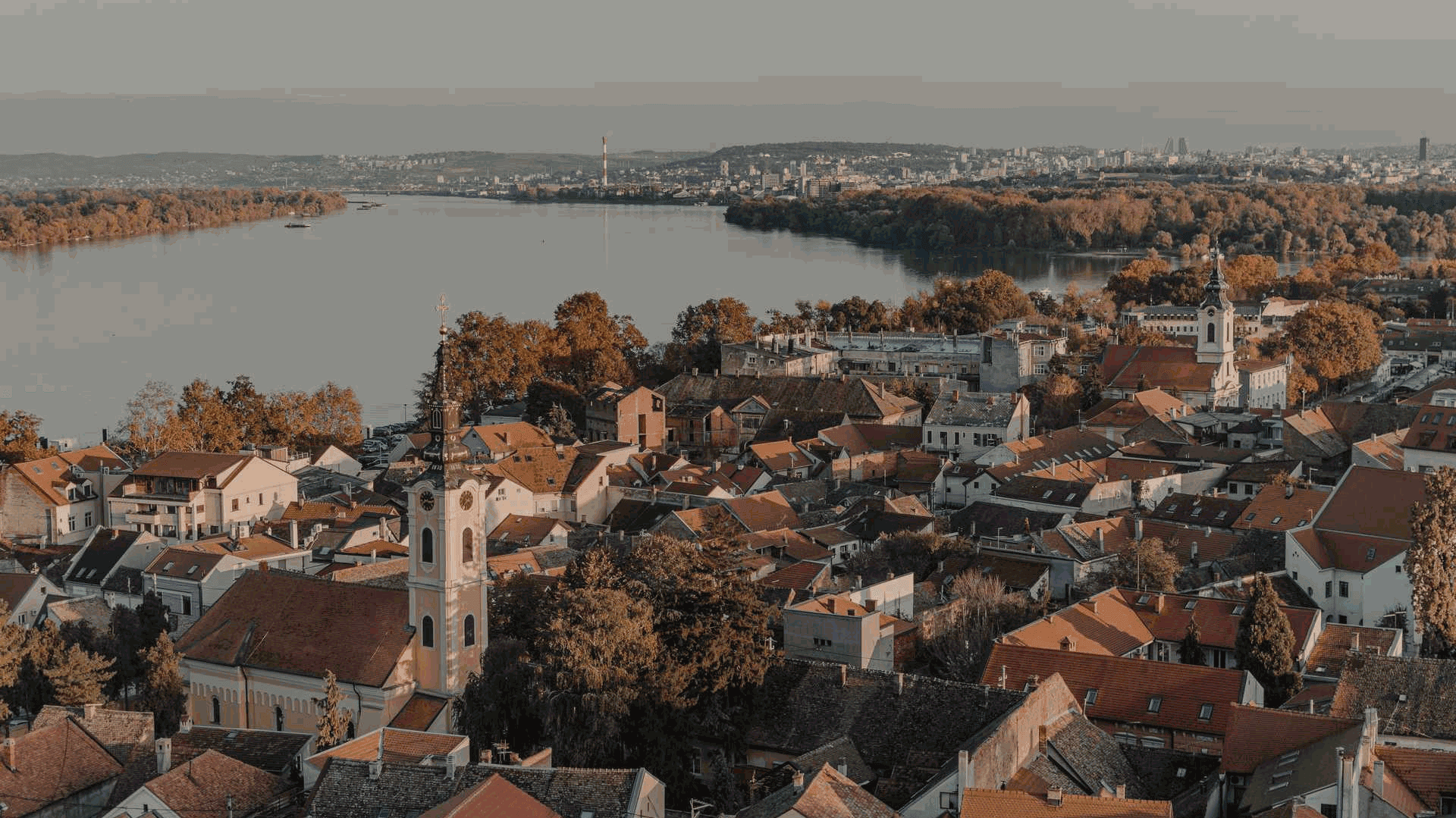 Panoramatický pohled na město a řeku za denního světla, červené střechy domů, podzimní krajina.