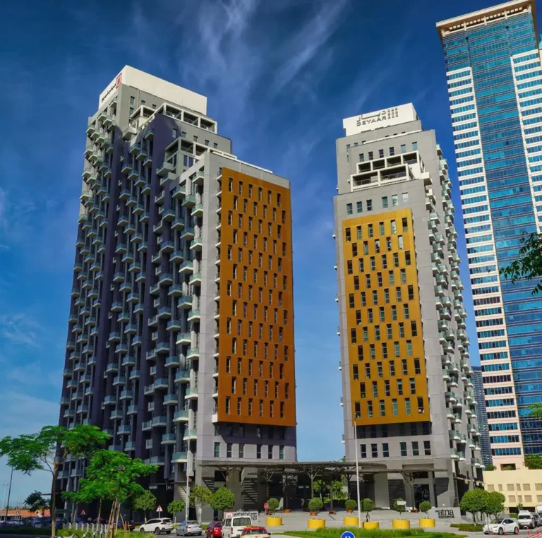 Dos modernos rascacielos con fachadas de vivos colores sobre un fondo de cielo azul y entorno urbano.