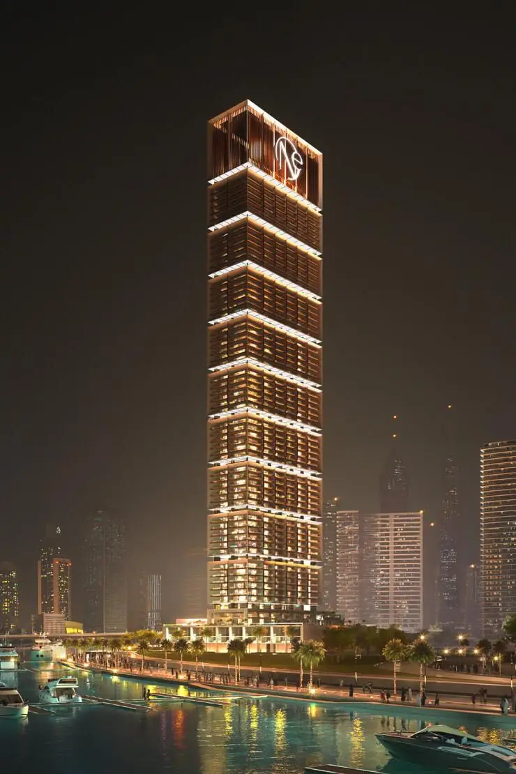 Edificio de gran altura con iluminación nocturna junto al agua, paisaje urbano moderno.