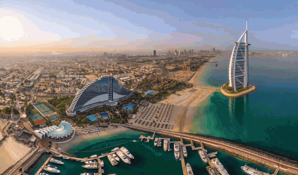 Vista do Burj Al Arab e das praias do Dubai a partir de cima. Sol sobre o mar e iates no porto.