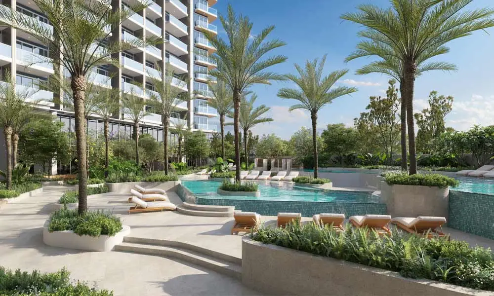 Pool and loungers in front of a modern building and palm trees on a sunny day.