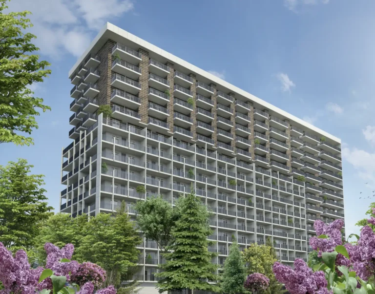 A modern residential complex next to green trees and flowering shrubs against a clear sky.