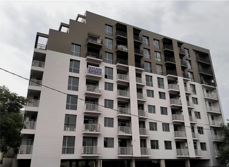 A multi-story residential building with balconies and gray facades against an overcast sky.