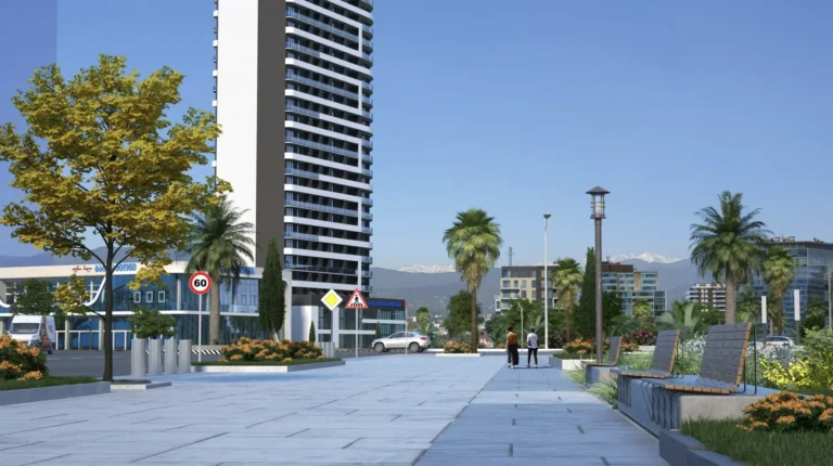 A modern street with a high-rise building, palm trees and mountains in the background on a sunny day.