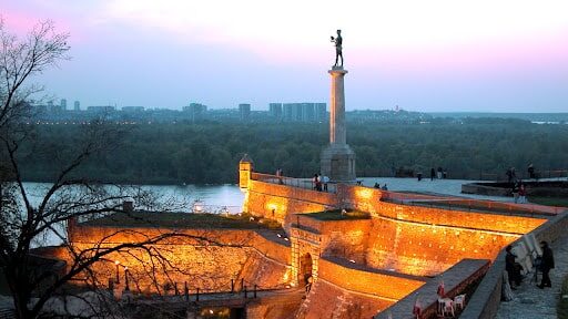 Fortaleza de Kalemegdan en Belgrado al atardecer, iluminada por las luces, con vistas al río y a la ciudad.