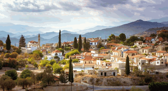 Un pintoresco pueblo de montaña con casas tradicionales y cipreses contra un cielo nublado.