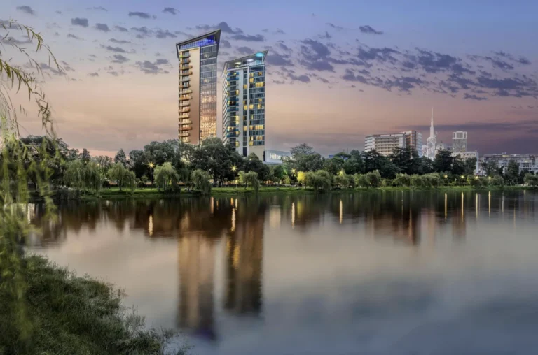 Modern cityscape with high-rise buildings by a pond at sunset.