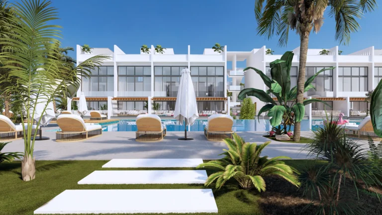 A modern hotel with a white facade, pool and sun loungers among palm trees against a sunny sky.