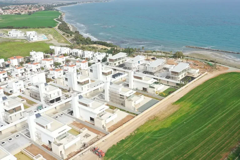 Un nuevo complejo residencial cerca del mar con un telón de fondo de campos verdes y la costa, una vista con muchos edificios blancos.