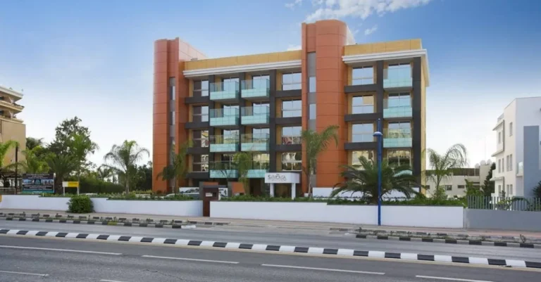 Un edificio moderno con grandes ventanales rodeado de palmeras contra un cielo azul.