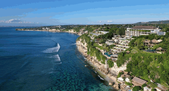 Una vista de la costa con acantilados y hoteles rodeados de naturaleza tropical, con el océano y el cielo despejado como telón de fondo.