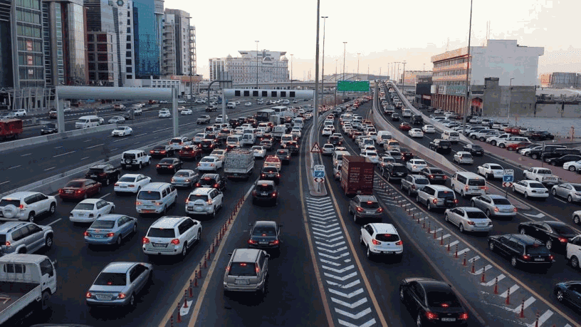 Dense city traffic during rush hour: cars fill the multi-lane road among high-rises and commercial buildings.