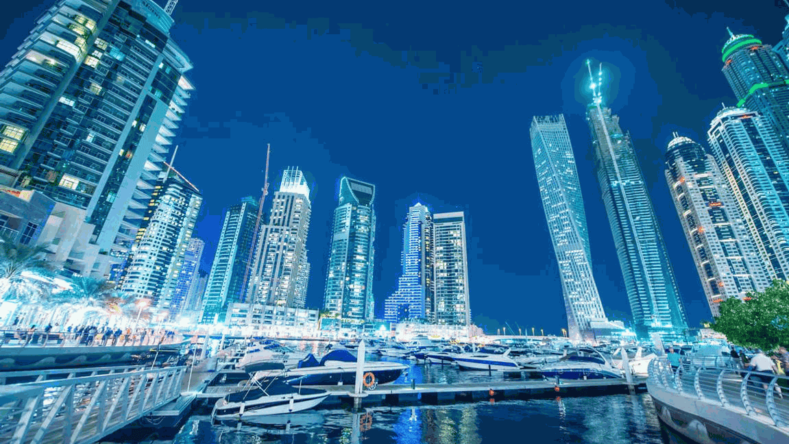 Modernos rascacielos y yates en el puerto deportivo de Dubai por la noche, iluminados por las brillantes luces de la ciudad.