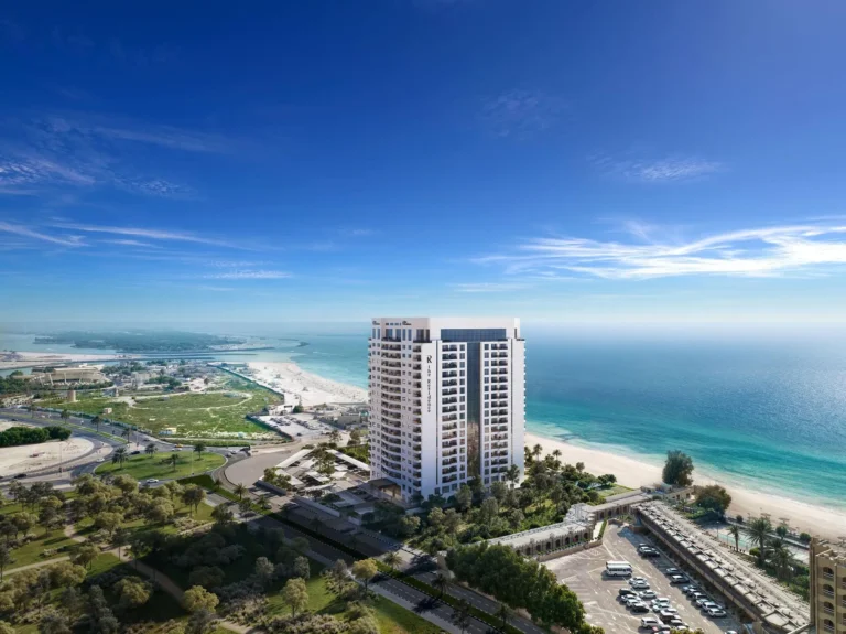 High-rise building by the sea overlooking the beach and city infrastructure under clear skies.