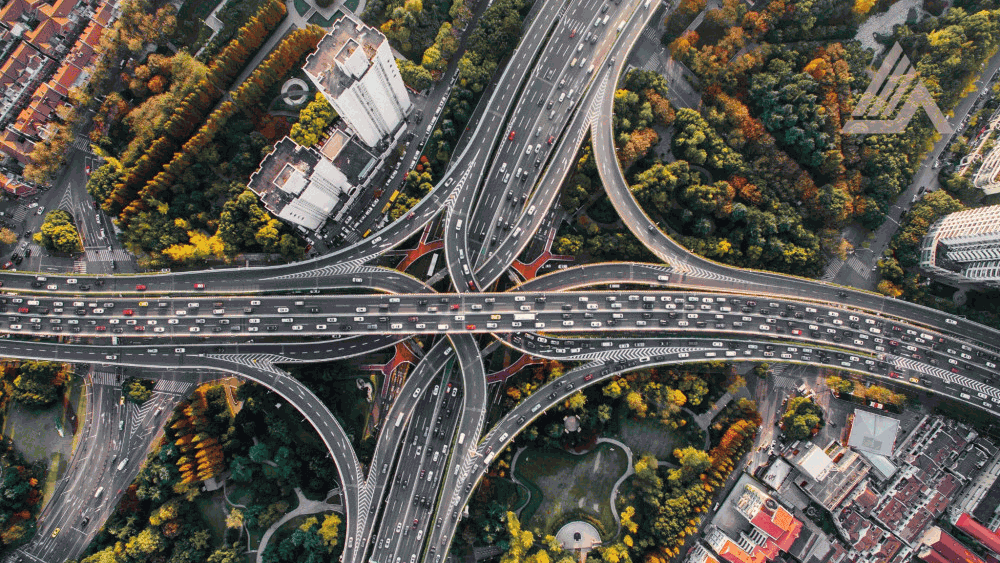 Aerial view of a complex transportation interchange in an urban landscape with green areas and buildings.