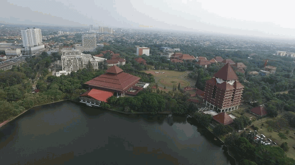 Imagen de un edificio universitario de tejados rojos cerca de un lago y un paisaje urbano a lo lejos.