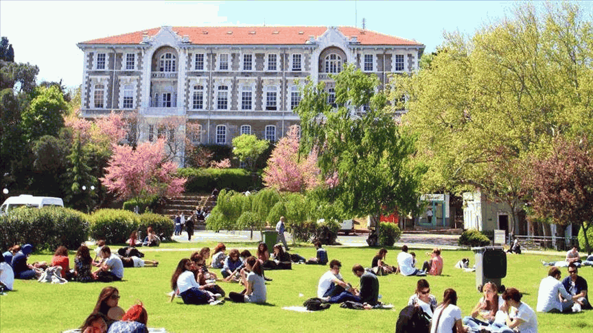Students relax on the grass in front of the university building on a spring day.